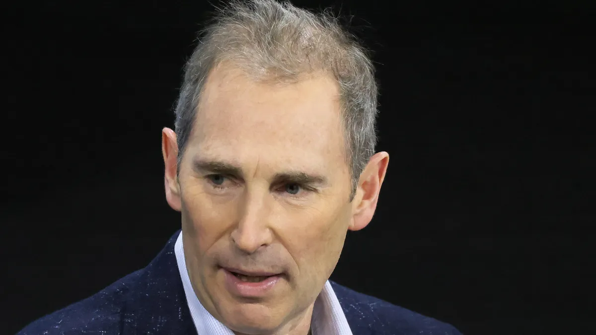 A man in a navy blazer and blue button down shirt against a black background