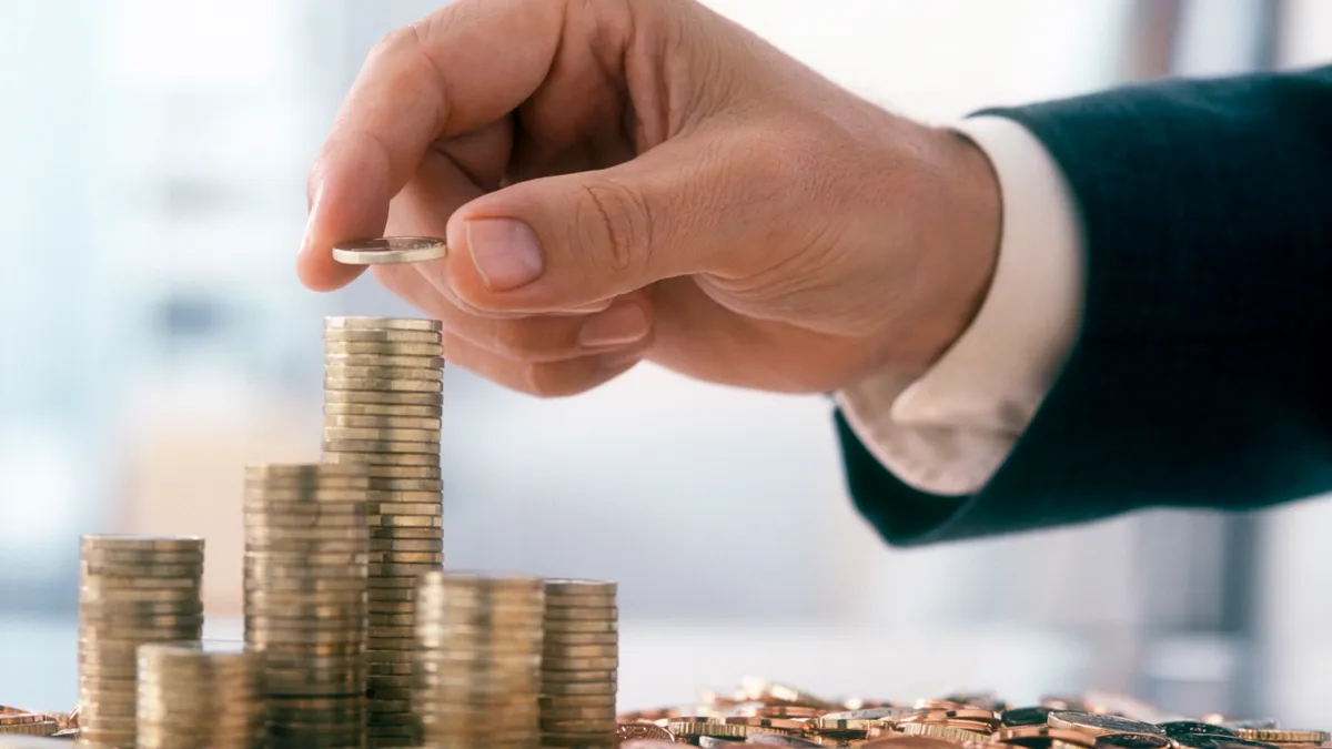 Hand of a mid adult man, wearing a siut, is stacking coins.