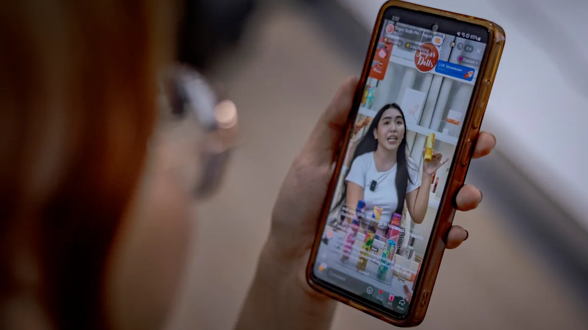 A person holds a smartphone depicting a person holding a skincare product.